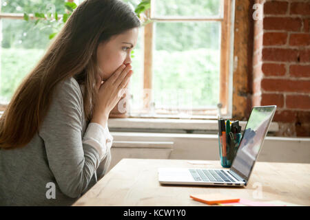 Shocked young woman looking at laptop screen at work desk. Casual business lady in office seeing something unbelievable on computer. Bad news concept, Stock Photo