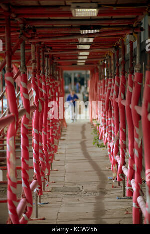 scaffolding red tunnel girl man in distance walking through viewed from behind city scene street Stock Photo