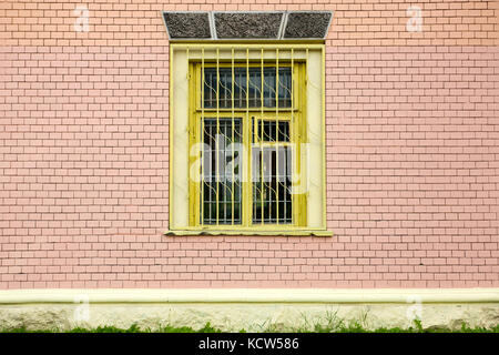 Yellow window with bars on a painted brick wall Stock Photo