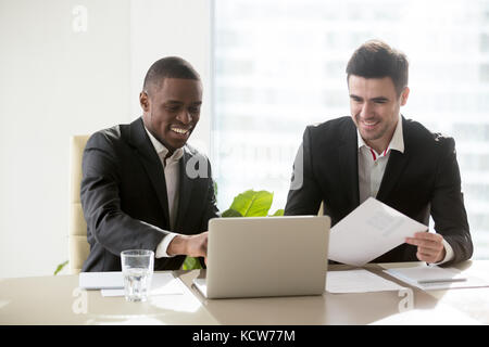 Happy multi-ethnic business partners satisfied after evaluating offer perspectives, smiling when analyzing company financial results. Afro american bu Stock Photo