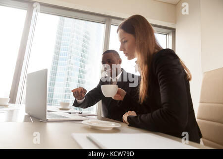 Afro american business adviser pointing on laptop screen at negotiations with white businesswoman in office. Multinational colleagues working on proje Stock Photo
