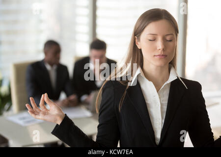 Portrait of attractive female office worker trying to keep calm in difficult situation at work. Businesswoman meditating with closed eyes, ignoring pr Stock Photo