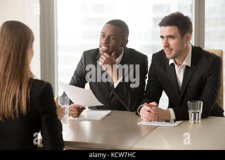 Afro american company leader with caucasian hiring manager listening and reviewing female job applicant after reading resume or CV. Multinational empl Stock Photo