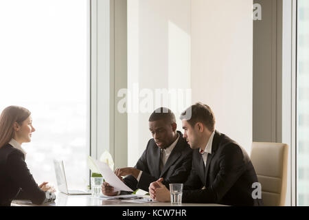 African american employer discussing candidates resume with caucasian colleague, reading and pointing on important CV information. Nervous young femal Stock Photo