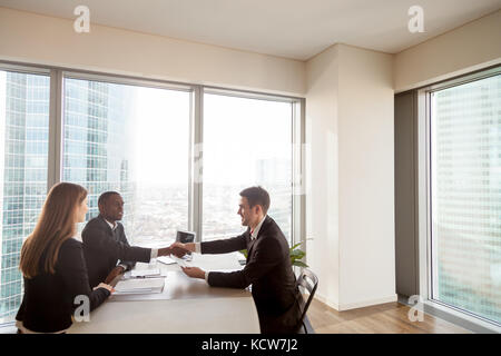Satisfied multinational business partners celebrating successful negotiations, deal conclusion, profitable agreement. Afro american HR leader handshak Stock Photo