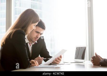 Caucasian female and male recruiters carefully reading african american candidate resume, business partners analyzing agreement document, studying imp Stock Photo