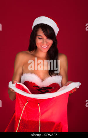 Young Happy Woman Looks Into A Santa Bag Over Red Background Stock Photo