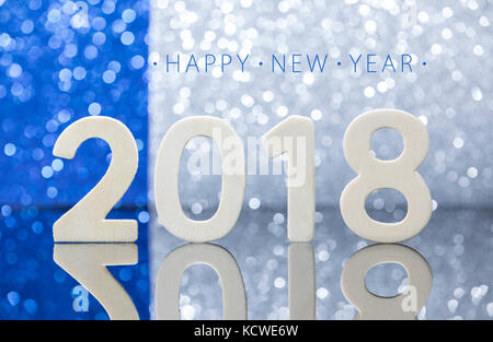 New year 2018 white wood numbers reflexion on glass table in front of the blue and silver lights bokeh. Stock Photo