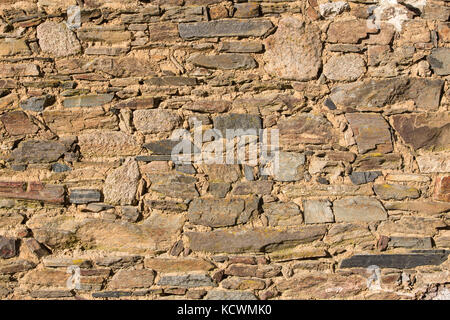 Brownish stone patterns on an old dry stone wall lit by the  afternoon sun. Stock Photo