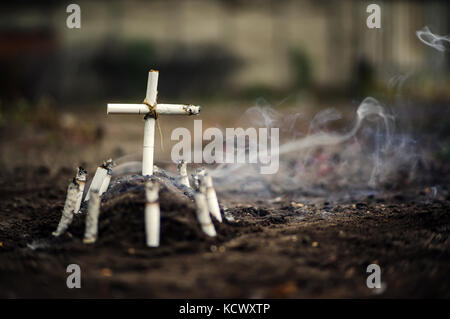 Grave of bad habit. Anti tobacco a conceptual photo with copyspace. Tomb with a cross made of cigarettes and cigarette butts on the ground. Stock Photo