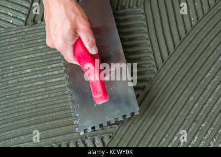 Close-up detail of floor tiles installation. Home improvement, renovation. Workers hand with notched float for tile. Ceramic tile floor adhesive, mort Stock Photo