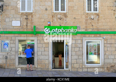 A tourist using an ATM outside an Otp Banka in Korcula Town, Korcula Island, Croatia, Dalmatia, Dalmatian Coast, Europe. Stock Photo