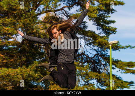 Stilish young man with a long beard and with a long hair who is jumping from the bridge  sunny day on summer. Stock Photo