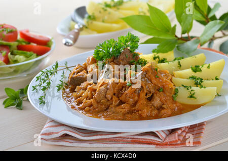 Typical Hungarian goulash (pork and beef) with pickled white cabbage (sauerkraut) and boiled potatoes Stock Photo