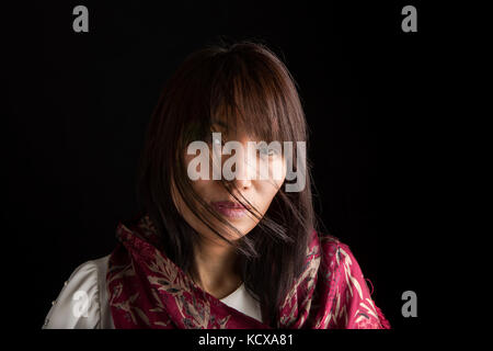 A close up low key portrait of a pretty Korean woman with a scarf. Stock Photo