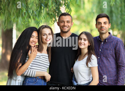 Five women and men friends on green forest background. Half body portrait of multi racial friends in park on summer sunny day. Beautiful happy carefre Stock Photo