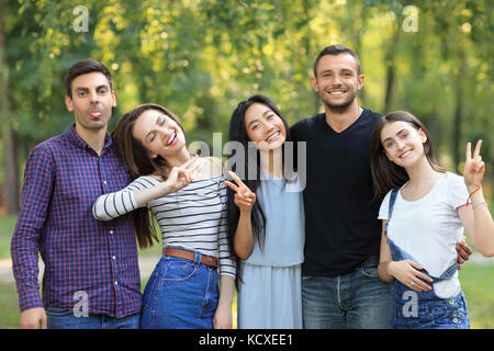 Happy friends men and women with facial expressions and gestures. Young cheerful people showing peace sign and tongue. Guy in black t-shirt expresses  Stock Photo