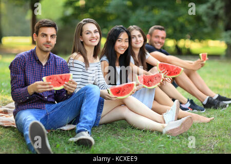 Five smiling women and men with slices of watermelon outdoors. Young friends students having fun at picnic with juicy fruit on warm day. Happy people  Stock Photo