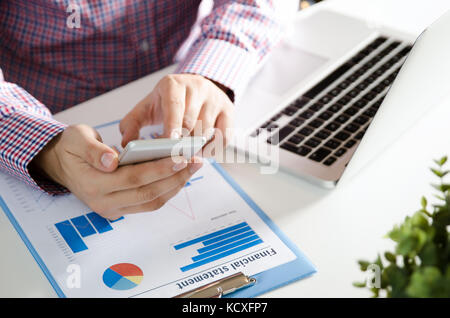 Man using mobile phone while working on laptop. Working with financial statement document Stock Photo