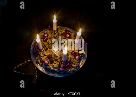 Advent wreath with four burning candles on a silver barrel, standing on  on a black table with glasses. Frederikssund, Denmark, Dec 30, 2016, Stock Photo