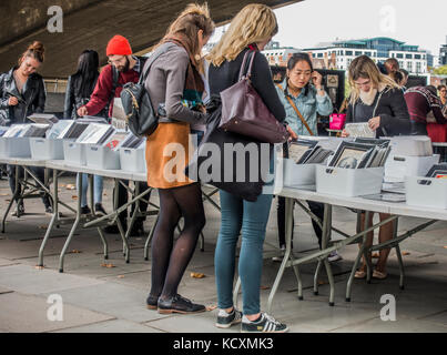 People browsing the range of books and prints at South Bank / Southbank book market, under Waterloo Bridge, next to River Thames, London, England, UK. Stock Photo