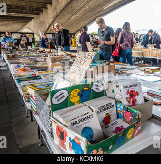 Mister Men books in the foreground, with people browsing at South Bank book market, under Waterloo Bridge over the River Thames, London, England, UK. Stock Photo