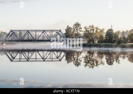 Railway bridge above misty lake. Reflection on water surface. Stock Photo