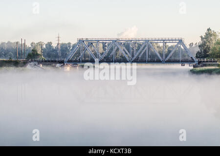 Railway bridge above misty lake. Reflection on water surface. Stock Photo