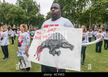 London, UK. 7th October 2017. People stand in a diamond formation dressed in t-shirts against the ivory trade and a man holds a graphic poster of a dead elephantwithout tusks in a half hour long silent protest in Parliament Square as an event in the annual Global March for Elephants and Rhinos (GMFER) taking place around the world. Speakers at the end of this vigil called on the UK government to bring in a full ban on ivory and end the trade by antiques dealers in Britain that plays a major role in keeping ivory markets open and driving the poaching that threatens to make elephants and rhinos 