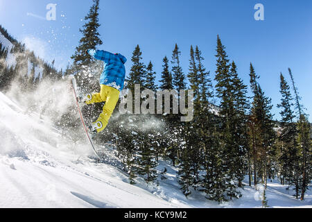 Snowboarder freerider jumping from a snow ramp in the sun on a background of forest and mountains.