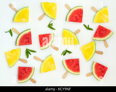 Red and yellow watermelon slices on wooden sticks with mint leaves among them on a white background. Flat lay, top view, copy space Stock Photo