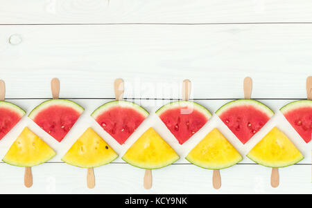 Red and yellow watermelon slices on wooden sticks on a white wooden background. Flat lay, top view, copy space Stock Photo
