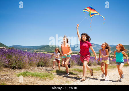 Group of happy age-diverse kids flying colorful kite running through lavender field Stock Photo