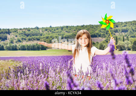 Portrait of beautiful preteen girl playing with colorful pinwheel in lavender field in summer Stock Photo