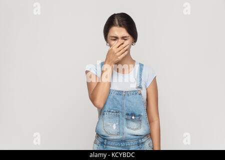 Unhappy and depressed young adult  gypsy woman, feeling ashamed or sick, covering face with both hands, keeping eyes closed. Isolated studio shot on g Stock Photo