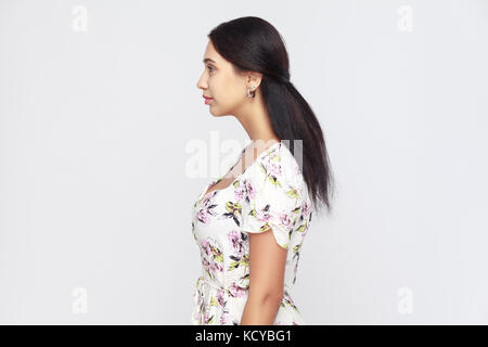 Side view of beautiful young adult woman, standing alone at gray background. Studio shot Stock Photo