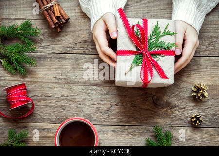 Christmas gift box with in female hands on wooden background, copy space. Decorated Christmas gift with fir branches for Christmas and winter holidays Stock Photo