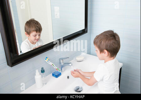 beautiful little boy washes his hands in blue bathroom Stock Photo