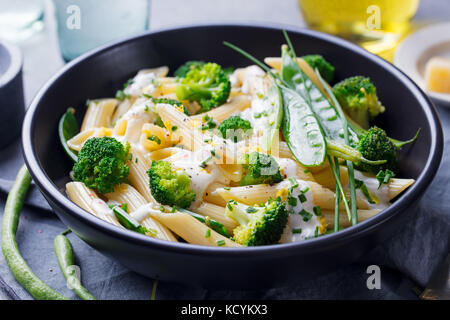 Pasta with green vegetables and creamy sauce in black bowl on grey stone background. Stock Photo