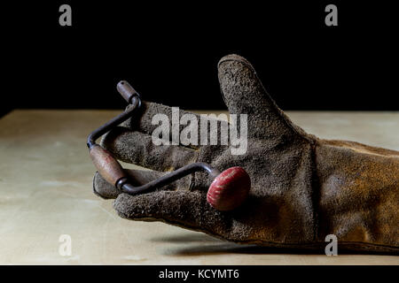 Hand in glove with tool for work in workshop. Hand protected by working coat. Workshop tool. Black background. Stock Photo