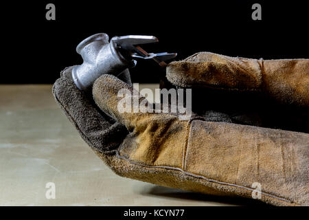 Hand in glove with tool for work in workshop. Hand protected by working coat. Workshop tool. Black background. Stock Photo