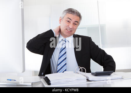 Mature Businessman Suffering From Neck Pain At Office Stock Photo