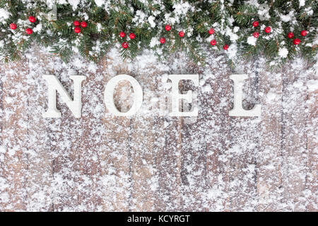 Christmas border out of snow covered natural Christmas tree fir twigs, red berries and noel written with white wood letters on a brown wooden backgrou Stock Photo