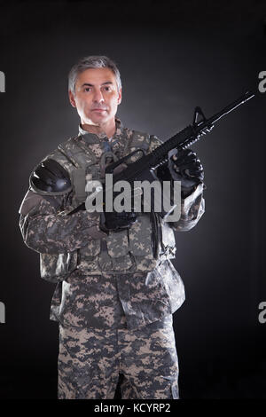 Portrait Of A Mature Soldier Holding Gun Over Black Background Stock Photo