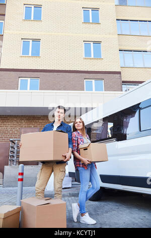Portrait of smiling young couple holding cardboard boxes posing outdoors while moving into new flat Stock Photo