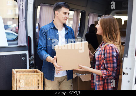 Portrait of smiling young man and woman unloading boxes from moving van outdoors Stock Photo