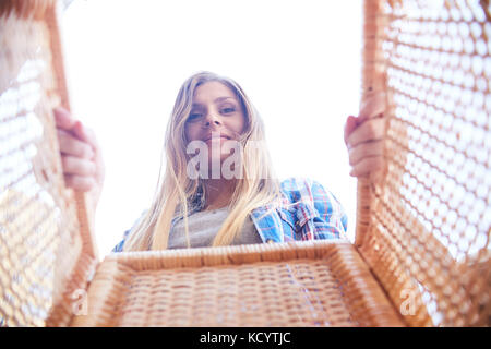 Portrait of happy young woman looking into wicker basket and smiling, shot from inside the box against white sky Stock Photo