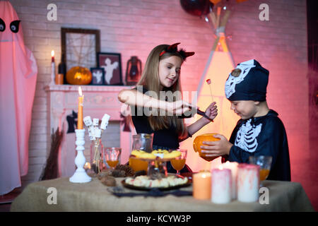 Portrait of children in Halloween costumes playing with carved pumpkin in decorated room during party Stock Photo