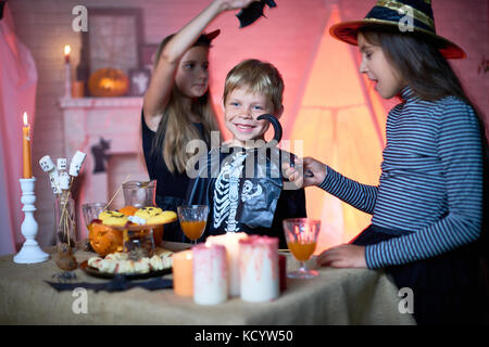 Portrait of children wearing Halloween costumes playing in decorated room during party, standing by table with food and sweets Stock Photo