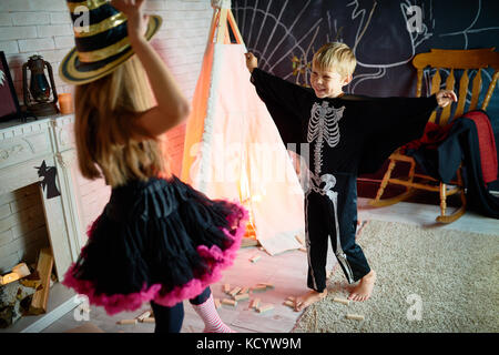 Portrait of two kids wearing Halloween costumes having fun playing in decorated studio Stock Photo